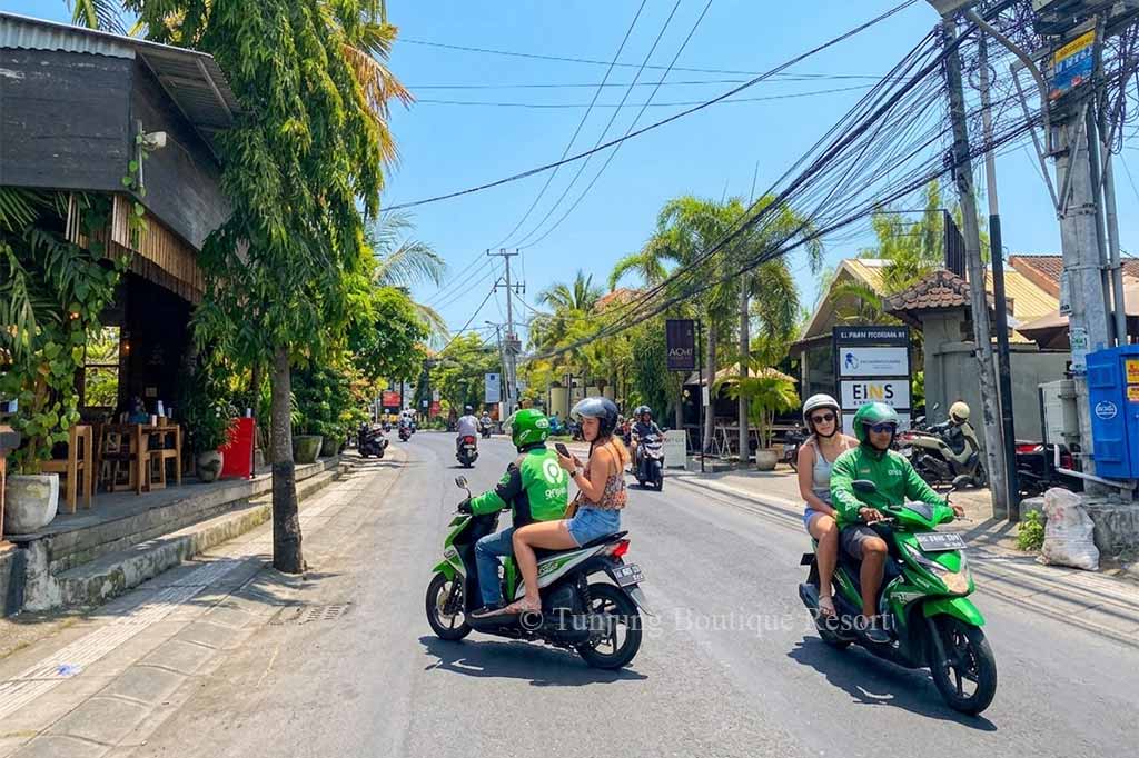 Foreign tourists riding on official Gojek and Grab motorbikes on a sunny day in Canggu Bali.