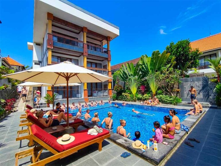 A large group of international tourists relaxing, swimming, and soaking in the sun at Tunjung Boutique Resort pool in Canggu during a bright day.