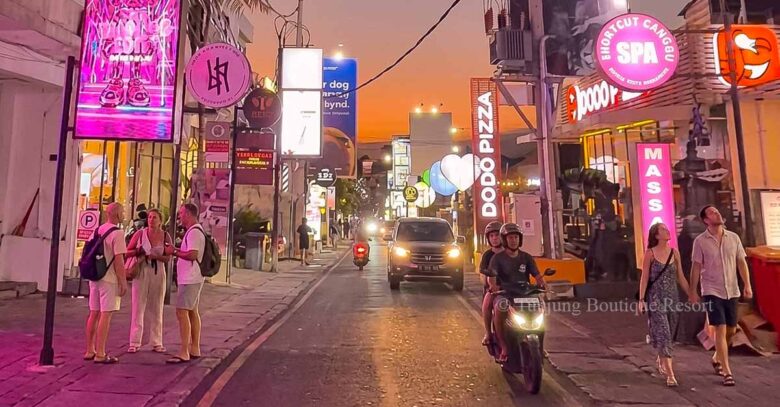 Canggu night streets illuminated by romantic pink neon lights with tourists walking along the sidewalk.
