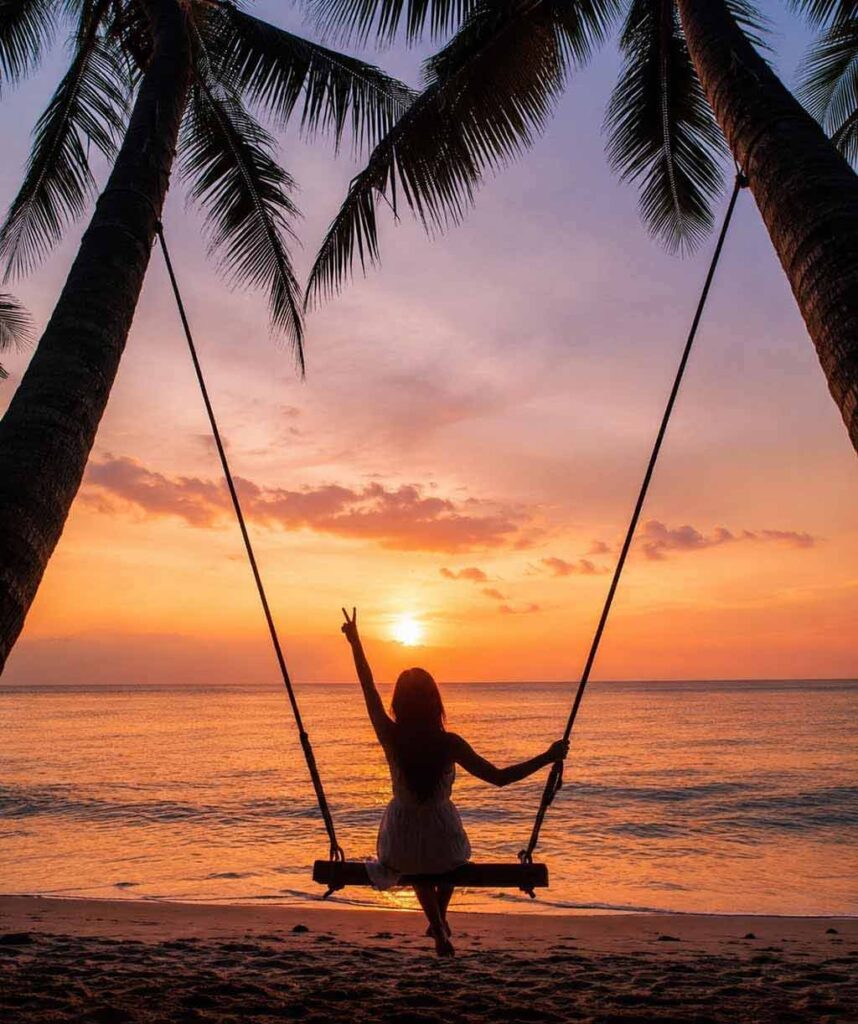 Woman on a beach swing at sunset