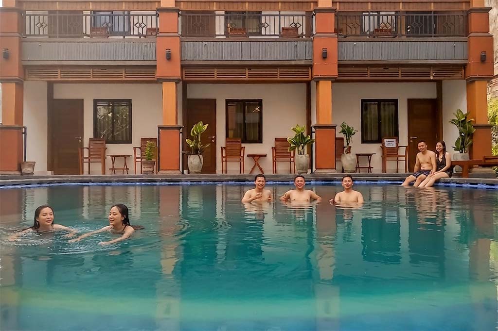 Asian travelers swimming and relaxing poolside at The Tunjung Boutique Resort during their stay in Canggu.