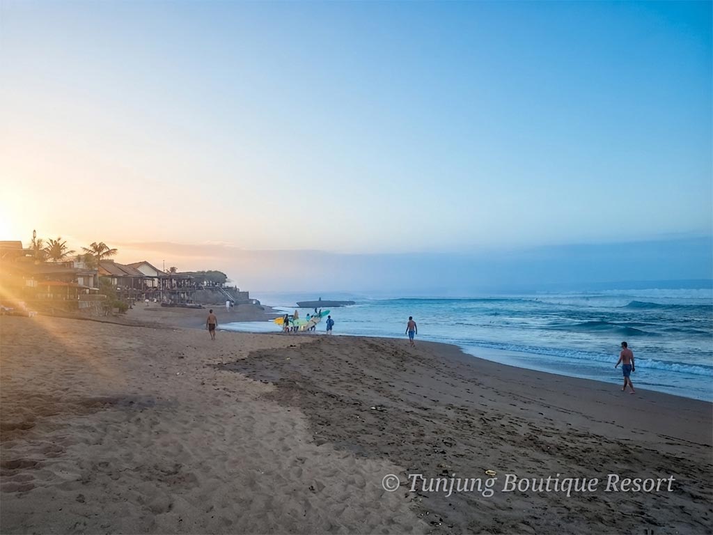 Bright morning atmosphere along Canggu beach with tourists walking by the ocean and surfers preparing to catch waves during a weekend in Canggu.