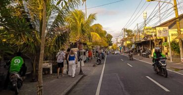 Bustling main street during a weekend in Canggu lined with stylish cafes, restaurants, and tourists walking along the sidewalk.