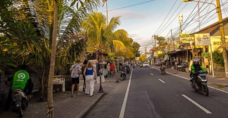Bustling main street during a weekend in Canggu lined with stylish cafes, restaurants, and tourists walking along the sidewalk.