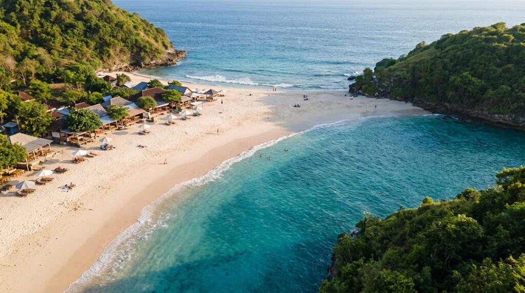 High aerial drone perspective of Virgin Beach in Karangasem, Bali, showing a sheltered crescent bay surrounded by lush green hills, white sand, and turquoise waters during late afternoon.