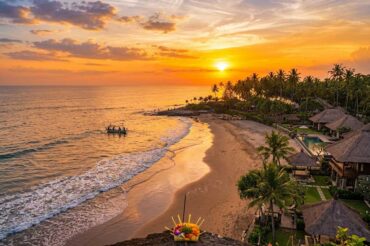An elevated view of seseh beach bali at sunset, showing black sand, ocean waves, coastal villas, and palm trees.