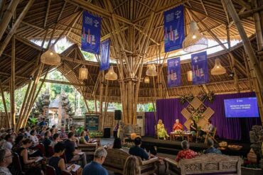 A lively panel discussion at the Ubud Writers & Readers Festival inside an open-air bamboo pavilion decorated with purple banners and woven lamps.