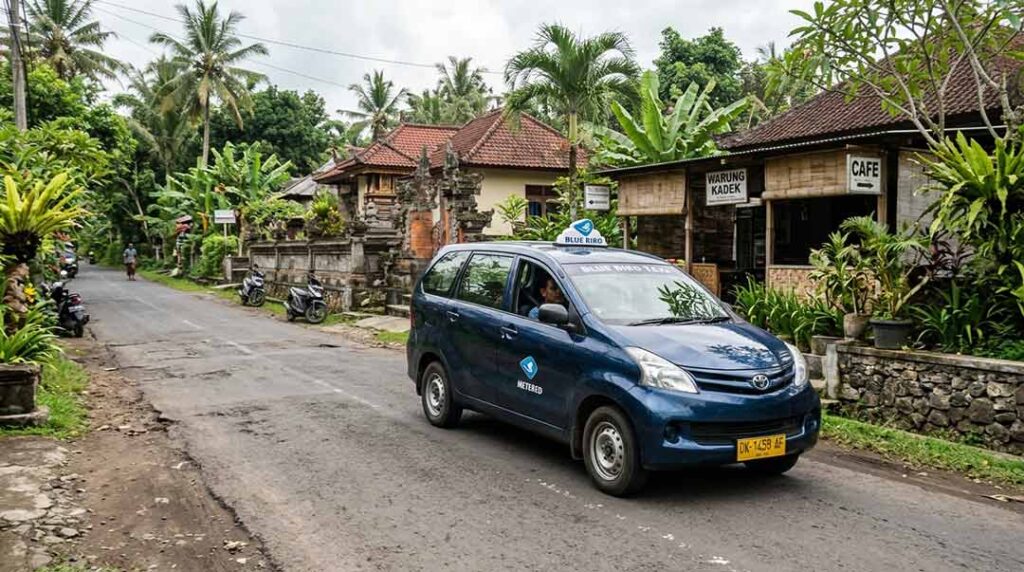 A traditional blue metered taxi driving along a quiet street lined with tropical greenery and local Balinese architecture.