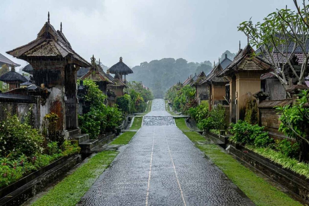 A wet stone pathway leading through Penglipuran traditional village in Bali on a rainy day.